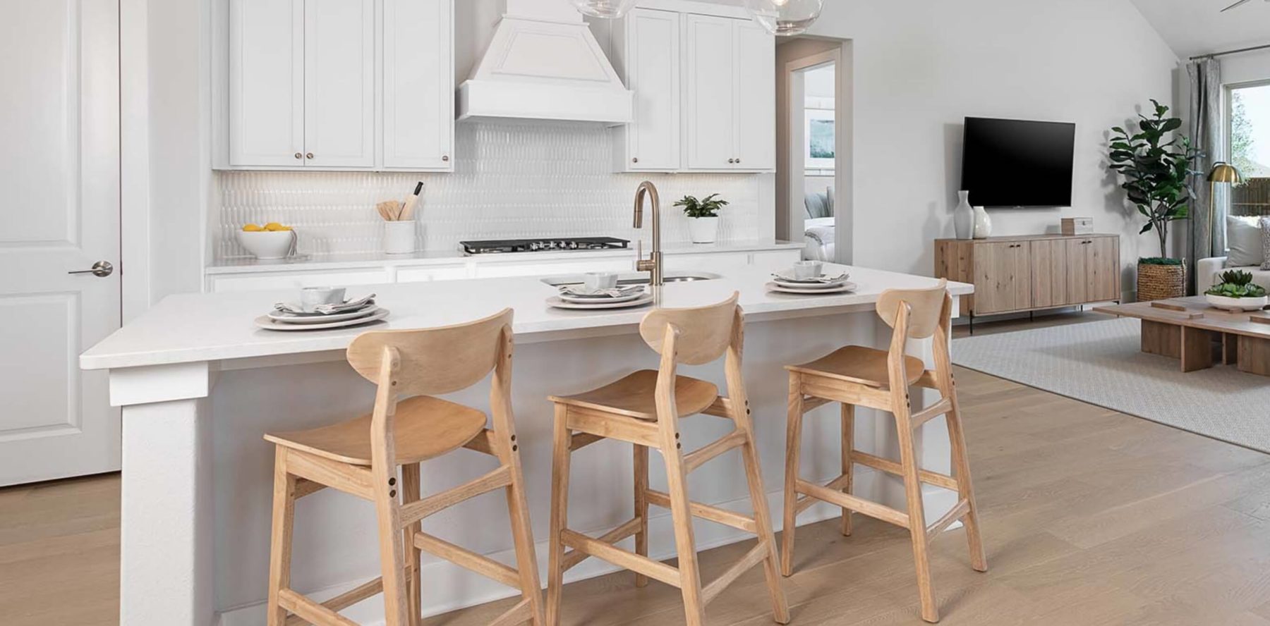 A white kitchen with wood stools and a TV in a new home.