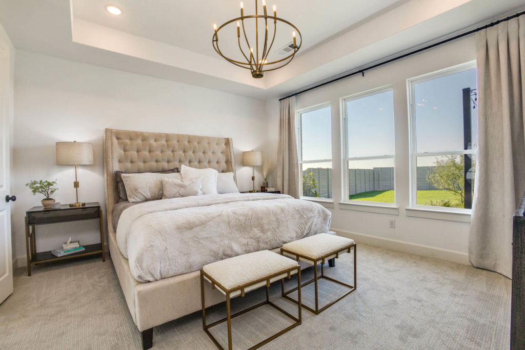 A bedroom in a McKinney home with a large bed and a chandelier, surrounded by the beauty of nature.