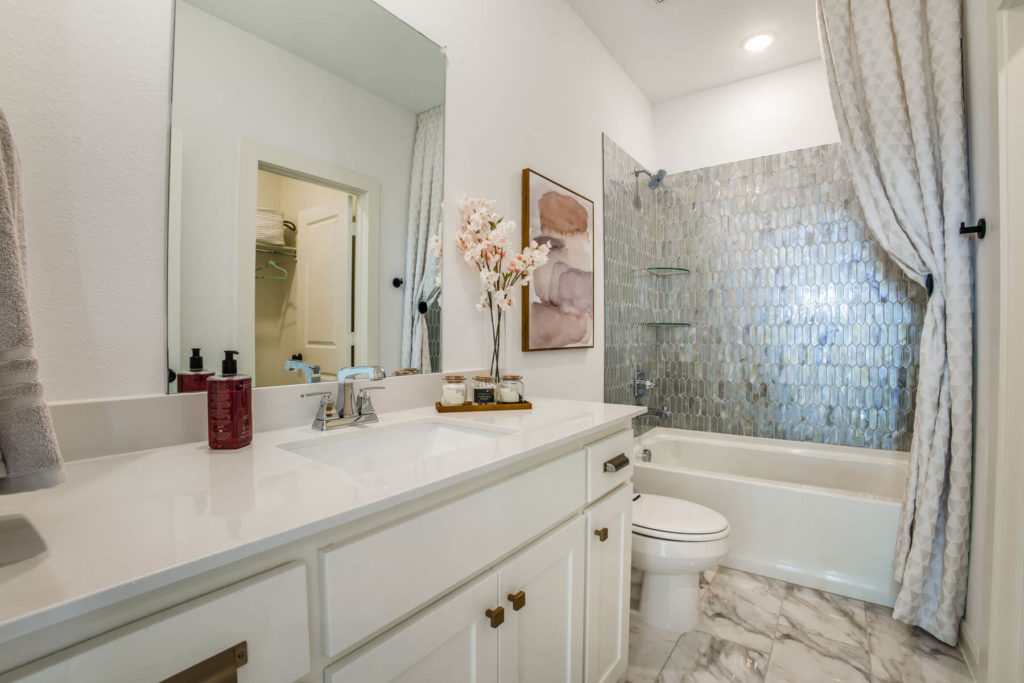 A bathroom in McKinney,Texas with white cabinets and marble counter tops, blending seamlessly with the surrounding nature.
