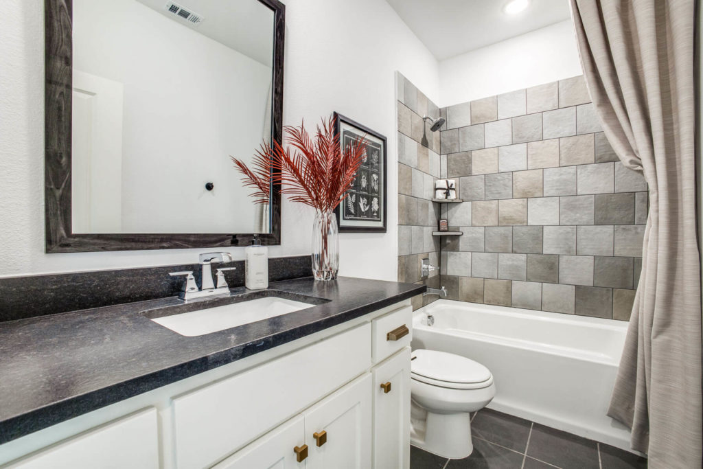 A newly built bathroom in a Texas home, featuring gray tile and black fixtures.