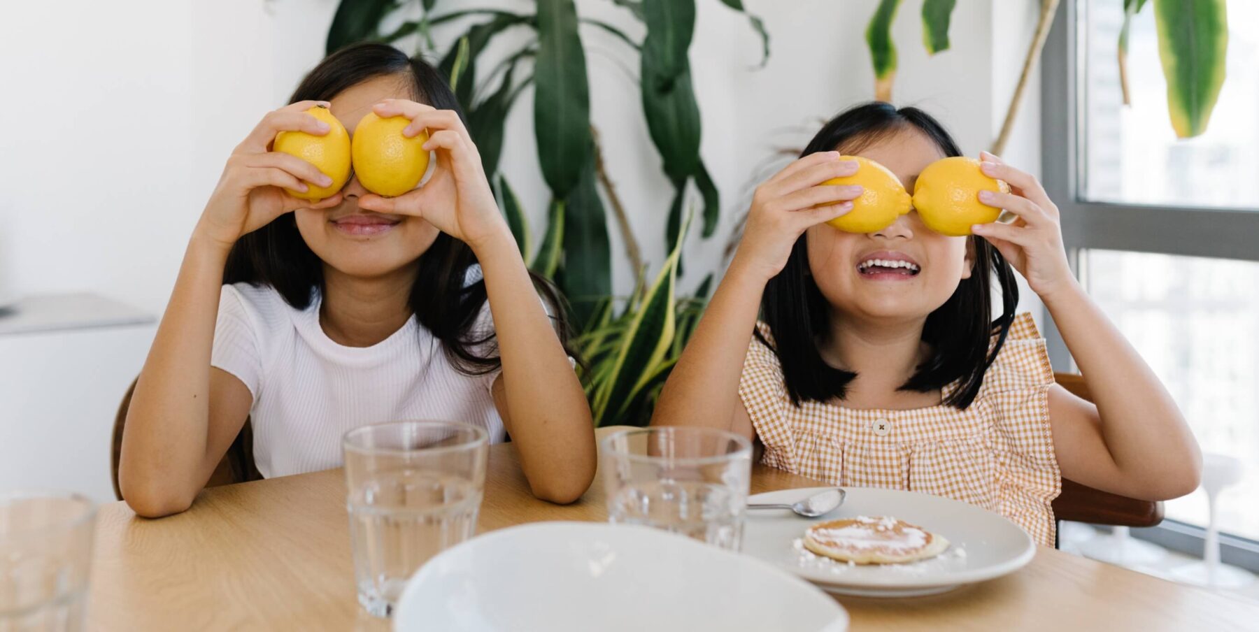 two young girls playing with their oranges at breakfast