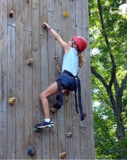 A girl climbing on a climbing wall in the woods surrounded by nature.