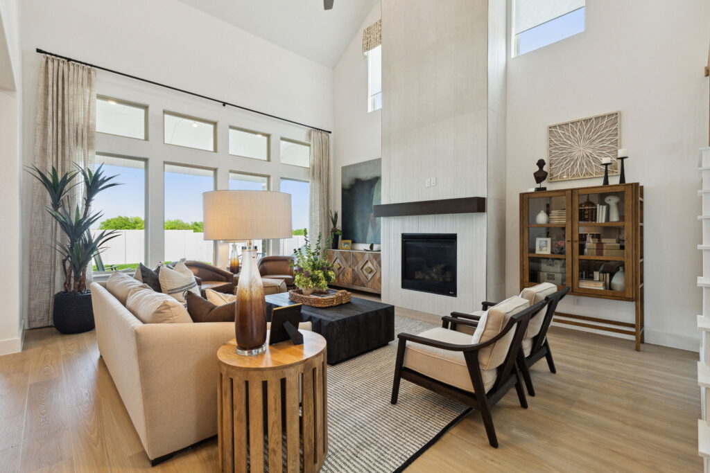 Modern living room in a McKinney Centre Living Home featuring high ceilings, large windows, a fireplace, and stylish furnishings including sofas and a bookshelf.