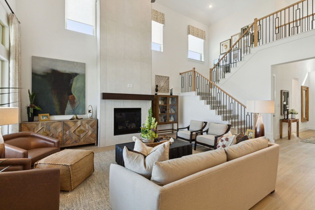 Spacious living room in a new home with high ceilings, modern furniture, a fireplace, and a staircase leading to the upper floor.