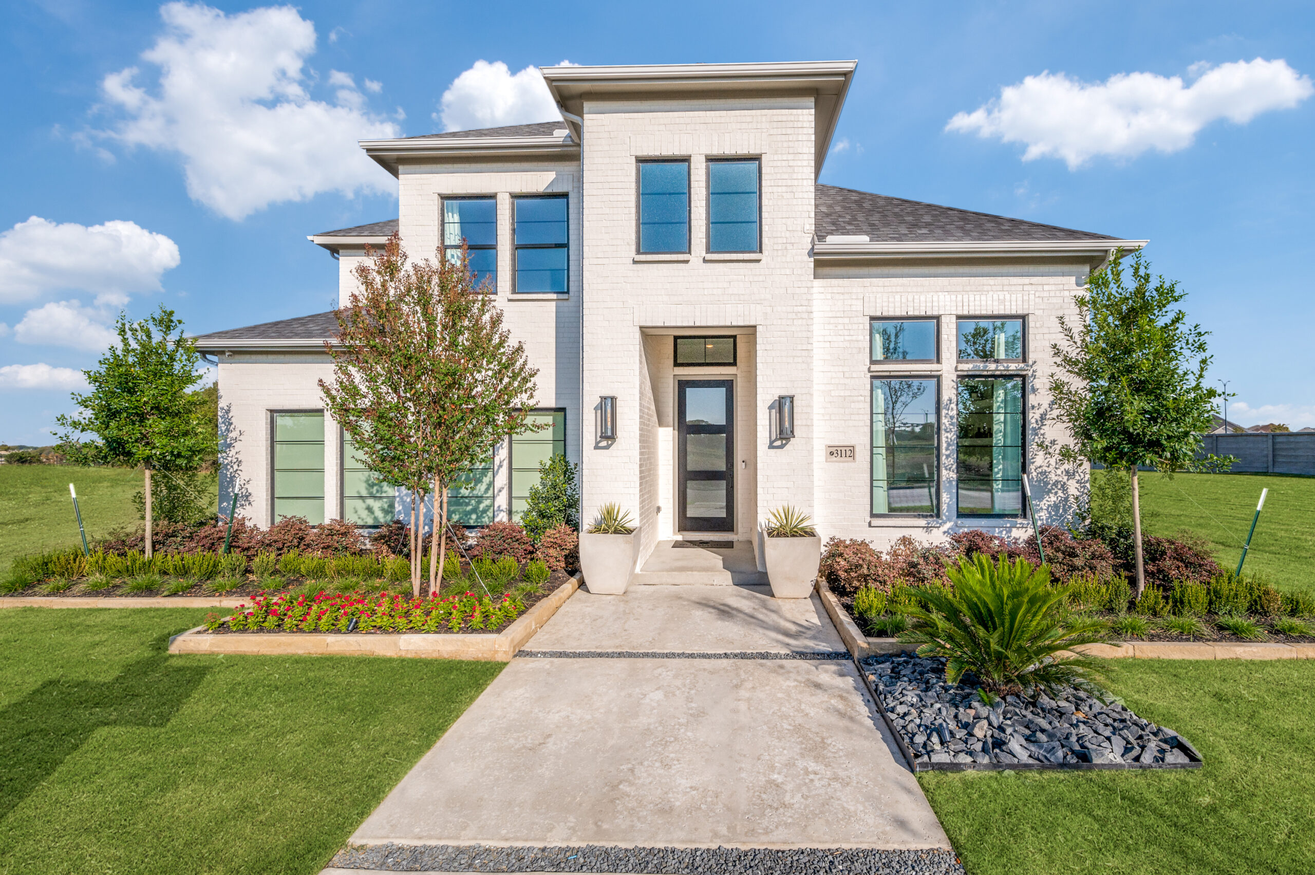 Modern two-story house with white brick exterior, large windows, landscaped front yard, and a concrete walkway leading to the front door—perfect for those seeking homes for sale in McKinney Texas or charming Painted Tree homes for sale.