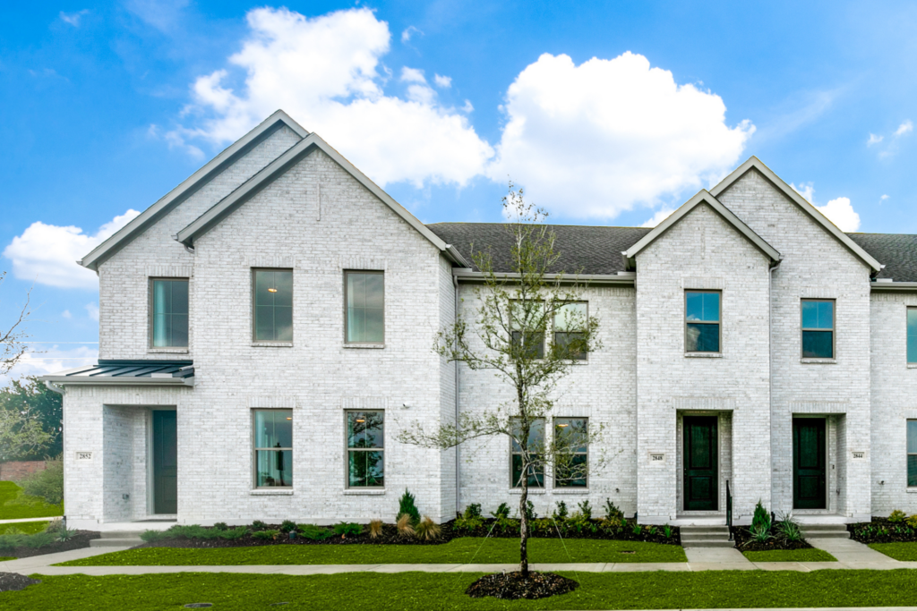 Modern white brick townhouse with multiple entry doors and windows, front lawn, young trees, and a clear blue sky—ideal for those seeking homes for sale in McKinney, Texas or exploring the latest Painted Tree TX communities.