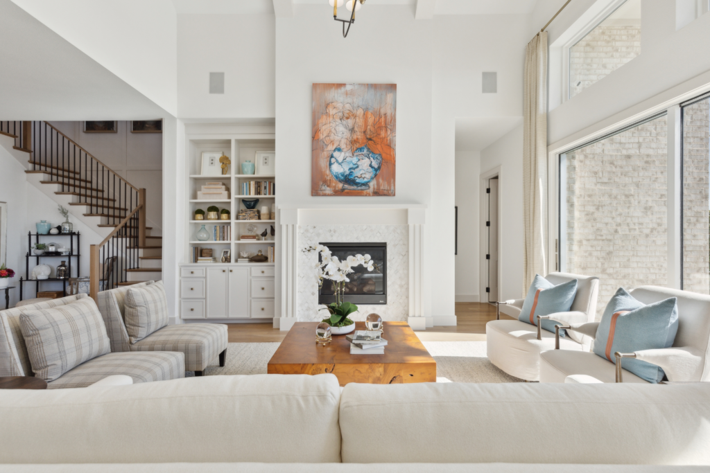 Modern open-concept living room in Painted Tree McKinney with a blue sofa, brown leather chairs, a striped armchair, and a kitchen featuring dark blue cabinets in the background—perfect for those seeking homes for sale in McKinney, Texas.