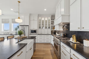 Discover a spacious modern kitchen by Southgate Homes featuring white cabinets, black countertops, and stainless steel appliances. Located in McKinney, TX, this stylish space boasts an island with a sink and elegant wooden flooring.