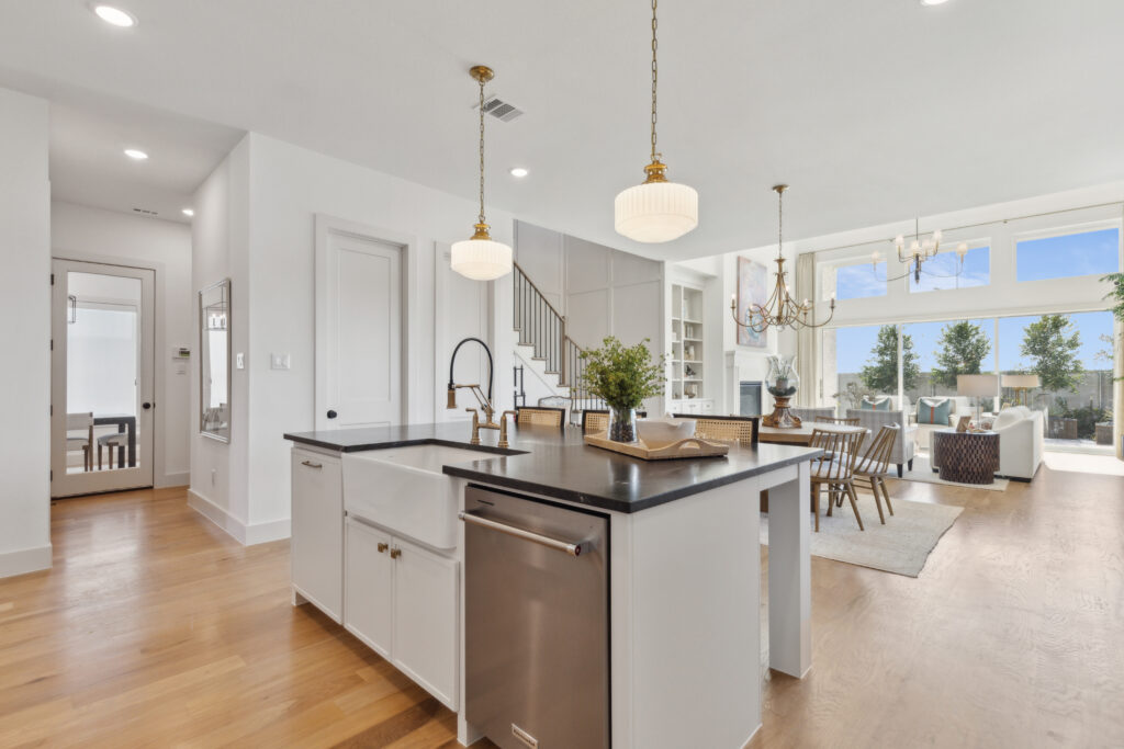 Experience the charm of a modern open-concept kitchen and living area by Southgate Homes in McKinney, TX. Revel in the wooden floors, a central island, and pendant lights illuminated by natural light from large windows. Stairs gracefully lead to an inviting upper level.