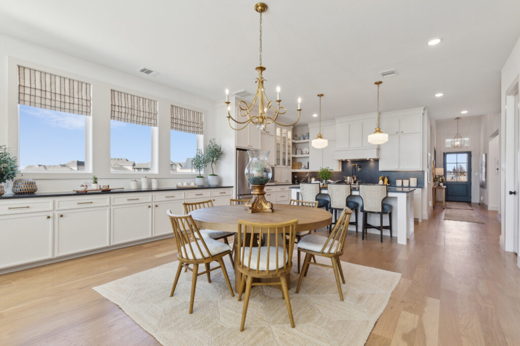 Discover a bright kitchen and dining area in one of the stunning Southgate Homes' new TX properties. Featuring a round wooden table, chairs, chandelier, and large windows above white cabinets, this home boasts a central island with stools and elegant overhead lighting.