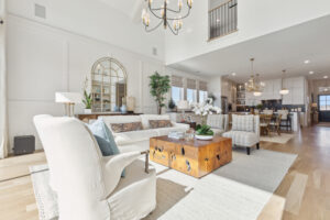 Located in McKinney, TX, this bright and spacious living room showcases light wood flooring, white walls, and modern furniture. Featuring a sofa, armchairs, a wooden coffee table, a chandelier by Southgate Homes, it offers a view into the dining area and kitchen.