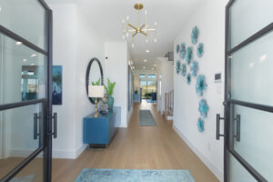 Modern entryway in a Drees Custom Homes design, featuring glass double doors, light wood flooring, blue console table with decor, wall art, and a view into a bright living space in the Painted Tree community of McKinney TX.