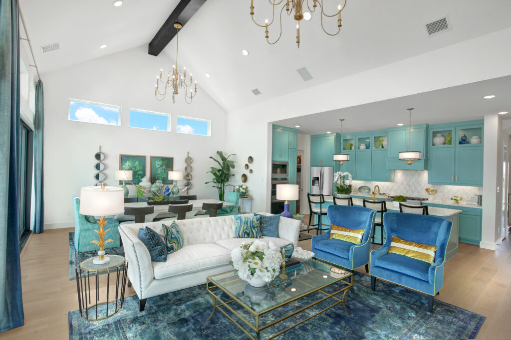 A spacious open-concept living and kitchen area with blue and white decor, modern furniture, high ceilings, chandeliers, and large windows letting in natural light awaits in this beautiful Drees Custom Homes new home for sale in McKinney TX.
