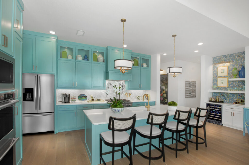 Modern kitchen in the Painted Tree community, McKinney TX, features turquoise cabinets, stainless steel appliances, island seating for four, pendant lights, and built-in shelving with decorative items.