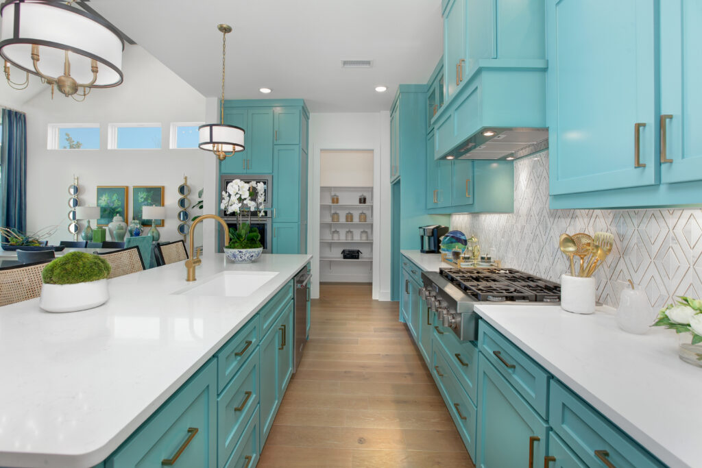 Modern kitchen with turquoise cabinets, white countertops, pendant lighting, gas stove, and hardwood flooring; open shelving and dining area visible in the background—perfect for a new home for sale by Drees Custom Homes in McKinney TX.