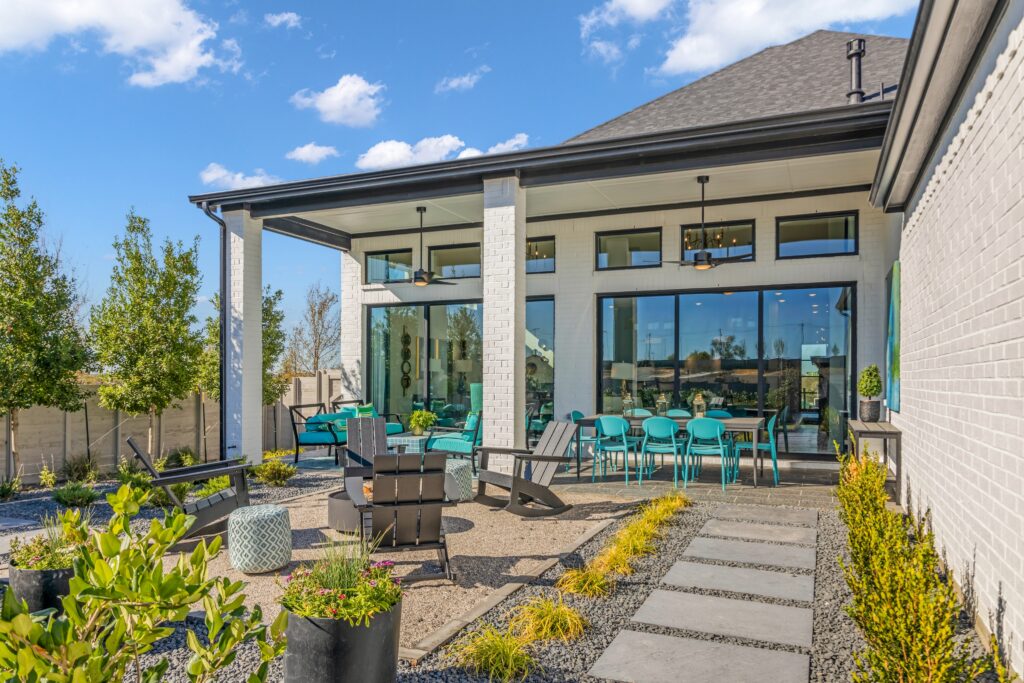 Modern patio with seating area, dining table, and glass doors. A stone path meanders through the landscaped garden of Drees Custom Homes. Under a clear blue sky, it's a perfect setting in the vibrant Painted Tree community for new homes in McKinney.