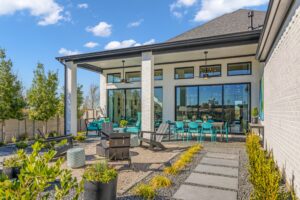 Modern patio with seating area, dining table, and glass doors. A stone path meanders through the landscaped garden of Drees Custom Homes. Under a clear blue sky, it's a perfect setting in the vibrant Painted Tree community for new homes in McKinney.