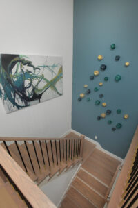 A modern staircase with wooden steps and railings, abstract artwork on one wall, and decorative wall-mounted objects on a teal accent wall in a beautiful new home for sale in the Painted Tree community, McKinney TX.