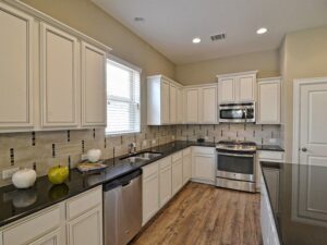 Modern kitchen with white cabinets, black countertops, stainless steel appliances, tile backsplash, and wood-style flooring—an inviting space found in many homes for sale in McKinney Texas, including the vibrant Painted Tree McKinney community.