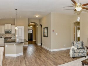 Open-concept living area with wood flooring, light beige walls, a ceiling fan, modern kitchen with island, and a hallway leading to the front door—experience comfort and style in Painted Tree McKinney homes for sale.