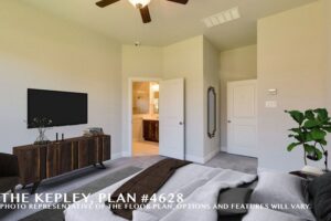 Bedroom with a bed in the foreground, TV on a wooden dresser, ceiling fan, potted plant, and open door leading to a bathroom. Discover comfort and style in Painted Tree McKinney—explore homes for sale in McKinney, Texas today!.