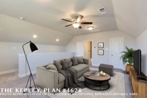 A modern loft living area with a gray sectional, round coffee table, TV, floor lamp, ceiling fan, neutral walls, and carpeted floors. Explore Painted Tree McKinney and homes for sale in McKinney Texas. Text reads "The Kepley Plan #4628.