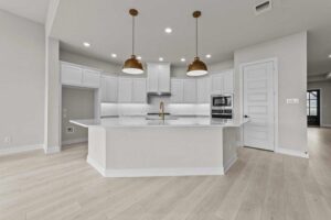Modern kitchen with white cabinetry, stainless steel appliances, gold fixtures, two pendant lights, and light wood flooring—perfect for those seeking Painted Tree McKinney style or exploring homes for sale in McKinney, Texas.