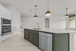 Modern kitchen in Painted Tree McKinney with a green island, built-in stainless steel appliances, pendant lights, white cabinetry, and light wood flooring—an inviting highlight among homes for sale in McKinney, Texas.
