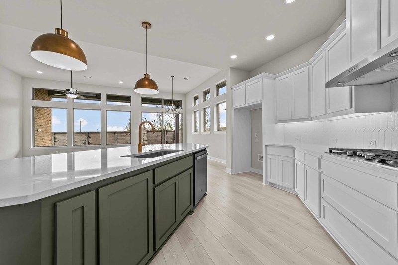 Modern kitchen with white cabinets, a large green island, pendant lights, built-in stove, and big windows letting in natural light—found in stunning Painted Tree McKinney homes for sale.