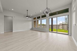 Modern empty living room with light wood floors, large windows, sliding glass doors to a backyard, and white walls—perfect for those seeking Painted Tree McKinney homes for sale. The space features two sleek ceiling light fixtures.