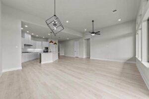 Open-plan room with light wood floors, white walls, modern kitchen with island, built-in oven, and pendant lights, plus large windows and a ceiling fan—perfect for those seeking homes for sale in McKinney Texas.