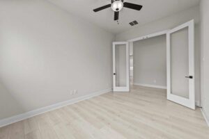 Bright empty room with light wood flooring, white walls, a ceiling fan, and double glass doors—perfect for those seeking homes for sale in McKinney, Texas.