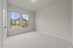 Empty room with light gray carpet, white walls, two windows with an outside view, and a closed white door on the left—perfect for those seeking comfort and style in Painted Tree McKinney homes for sale.