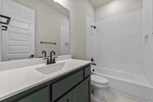 Modern bathroom with a white countertop, dark faucet and cabinet, large mirror, white toilet, and bathtub with black fixtures—perfect for those seeking stylish living in Painted Tree McKinney homes for sale.