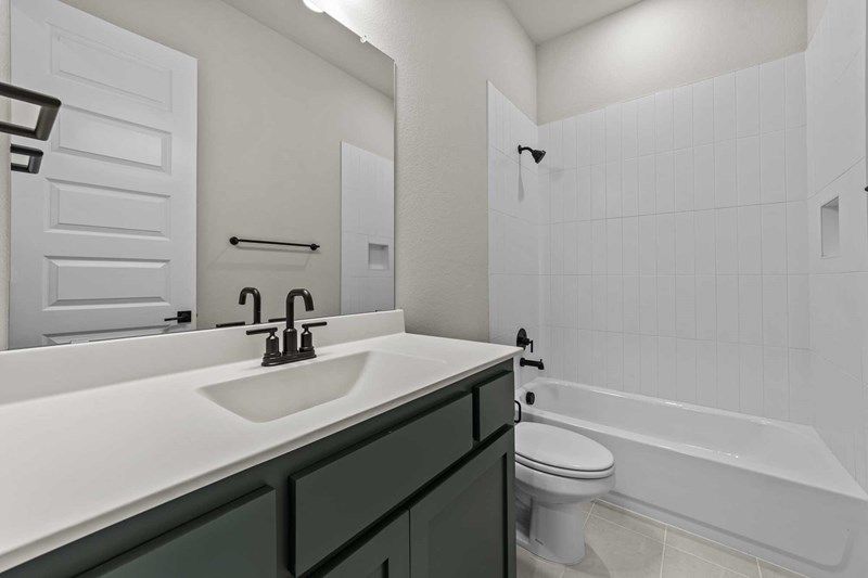 Modern bathroom with a white countertop, dark faucet and cabinet, large mirror, white toilet, and bathtub with black fixtures—perfect for those seeking stylish living in Painted Tree McKinney homes for sale.