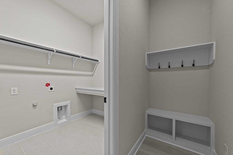 A laundry room with washer and dryer hookups, a countertop, overhead shelf, and an adjacent area with wall hooks and a built-in bench with cubbies—perfect for homes for sale in McKinney Texas.