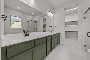 Modern bathroom in Painted Tree McKinney with green double-sink vanity, large mirror, black fixtures, and a walk-in closet. White tile floors and neutral walls complete this stylish space found in homes for sale in McKinney Texas.