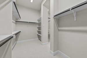 Spacious walk-in closet with multiple shelves and hanging rods, beige walls, and carpeted flooring—perfect for those seeking homes for sale in McKinney Texas or the beautiful Painted Tree McKinney community.