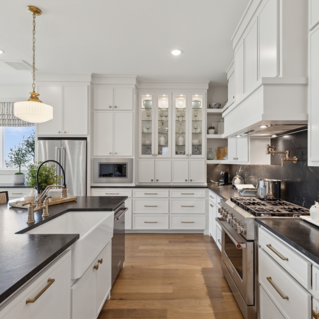 Discover a modern kitchen in one of McKinney's stunning new homes, featuring white cabinets, black countertops, stainless steel appliances, and a central island. The wood flooring and pendant lighting complete this TX treasure.