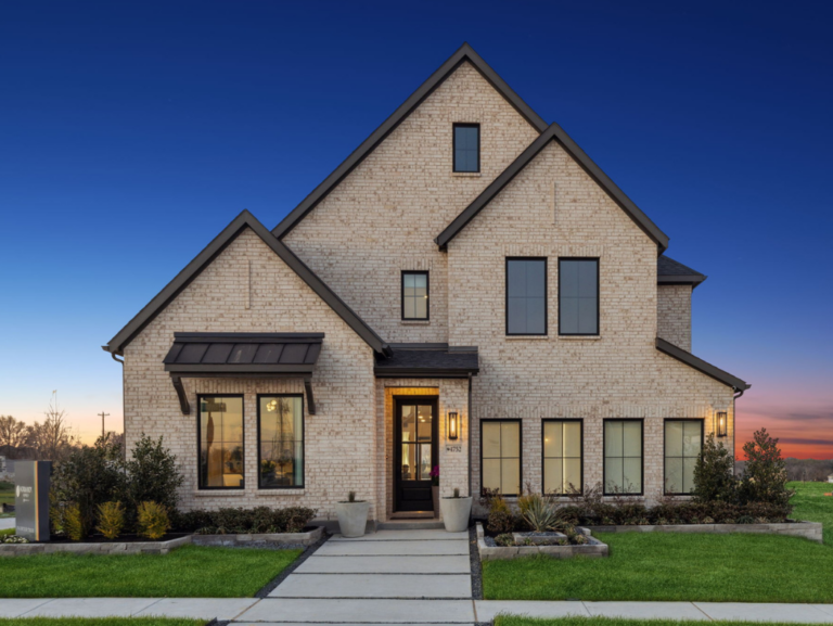 A modern two-story brick house in McKinney, TX, features large windows, a gabled roof, and a neat front lawn. The clear sky is tinged with the warm hues of sunset.