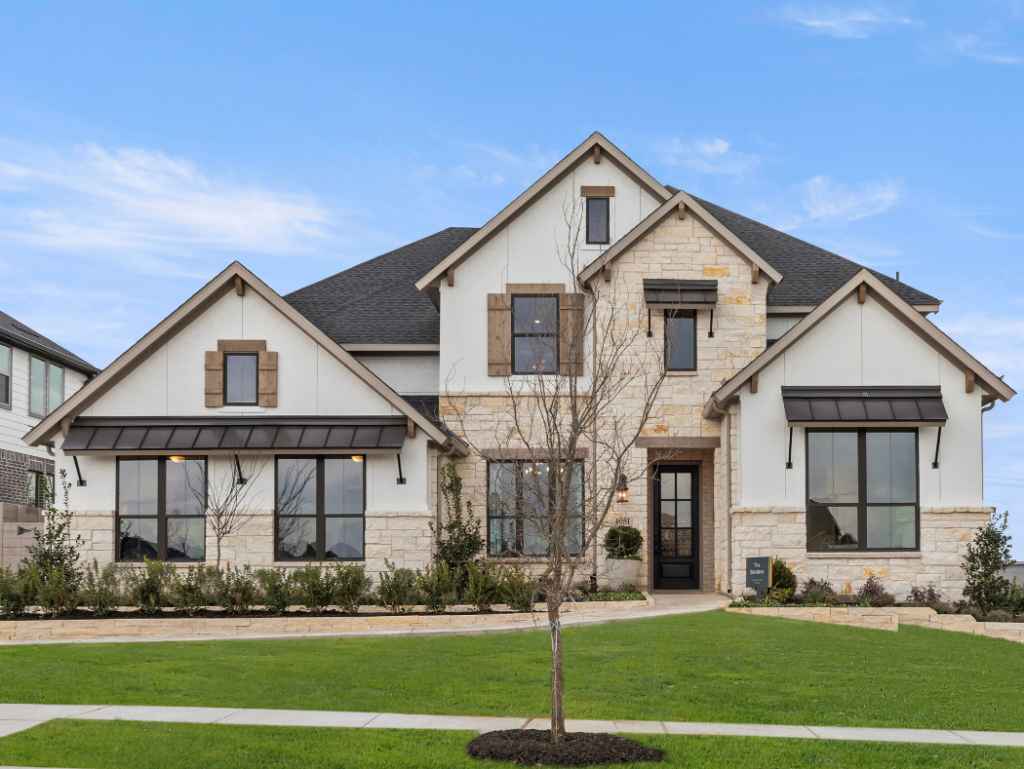 This two-story stone and stucco Coventry Homes residence in TX features a gray roof, multiple large windows, and a manicured lawn. Bare trees stand against the clear blue sky, harmonizing with its Painted Tree surroundings.