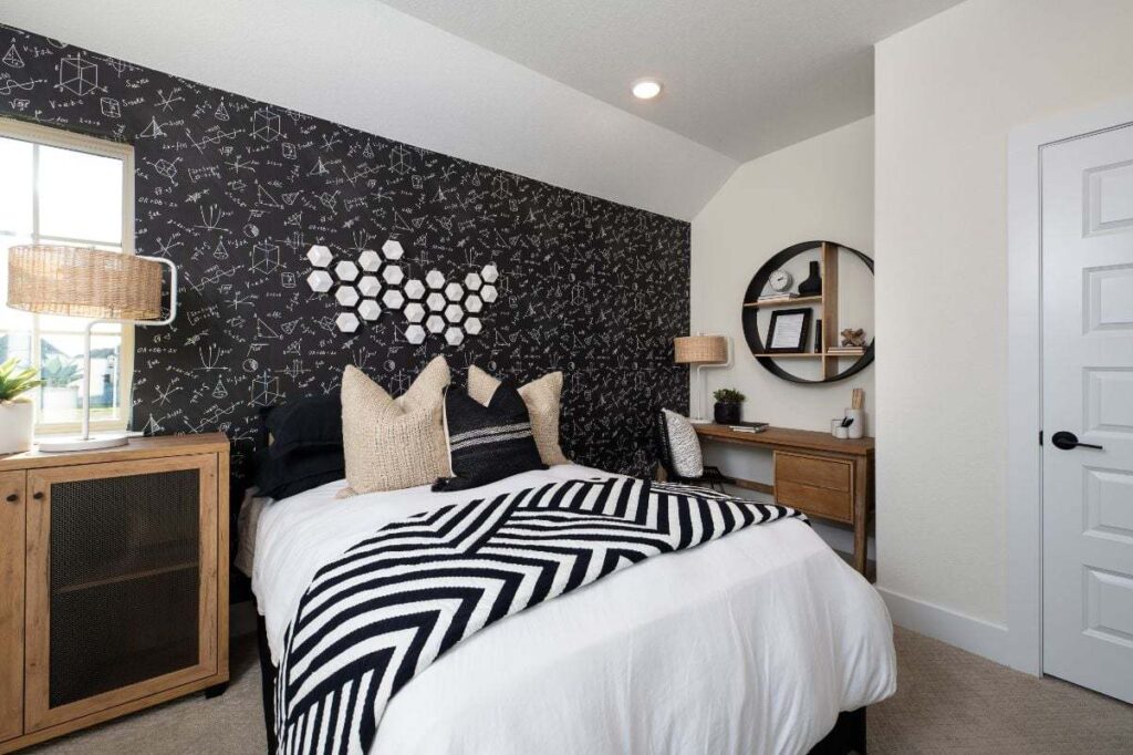 Modern bedroom with a black accent wall featuring constellations, a bed with black and white bedding, a wooden desk, round mirror, and neutral decor—perfect inspiration for those searching for homes for sale in McKinney Texas.