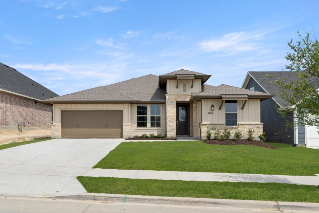 Single-story modern suburban house with a double garage, light-colored stone and siding exterior, small front porch, and a neatly maintained lawn in the sought-after Painted Tree McKinney community—explore homes for sale in McKinney, Texas today.
