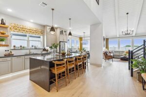 Modern open-concept kitchen and living area with light wood floors, a large black island with four wooden stools—one of the stylish features you'll find in Painted Tree McKinney homes for sale.