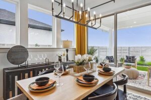 Modern dining room with a set table for four, large windows, gold curtains, chandelier, and a view of an outdoor patio—perfect for those seeking homes for sale in McKinney Texas or exploring Painted Tree TX.