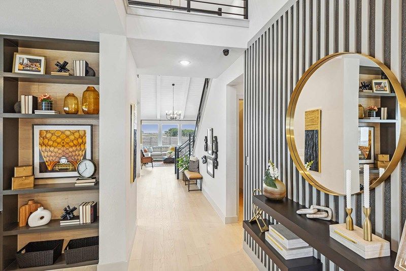 Modern hallway with built-in shelving on the left, a round mirror and decor on a black console table to the right, and a view into a bright living room—perfect for those seeking homes for sale in McKinney Texas.