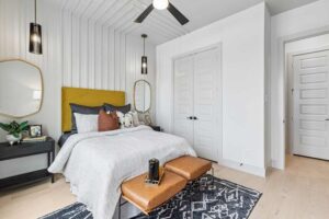 Modern bedroom with a yellow-accented headboard, neutral bedding, pendant lights, and double white doors—showcasing the stylish interiors found in Painted Tree McKinney homes for sale in McKinney, Texas.