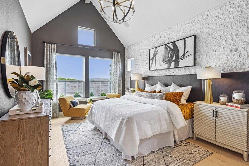 Contemporary bedroom with vaulted ceiling, large windows, white bedding, and modern artwork—an inviting retreat found in many Painted Tree homes for sale. A mustard-yellow accent chair by the window adds a pop of color to this stylish space.