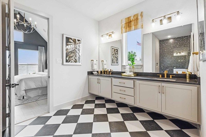 Modern bathroom with black and white checkered floor, double sink vanity with gold fixtures, large mirror, and a view into a bedroom—discover elegant details like this in Painted Tree McKinney homes for sale.