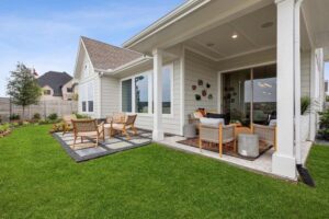 A modern backyard patio with outdoor seating, a covered area, decorative plants, and a manicured lawn next to a light-colored house in the sought-after Painted Tree McKinney community.
